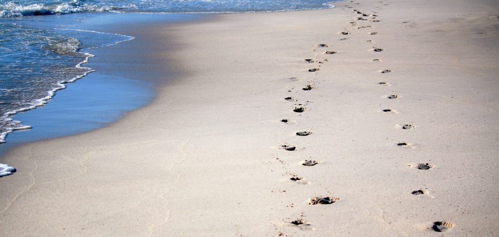 Tide coming in on a sunny beach. Footprint trail in the sand where people have been walking