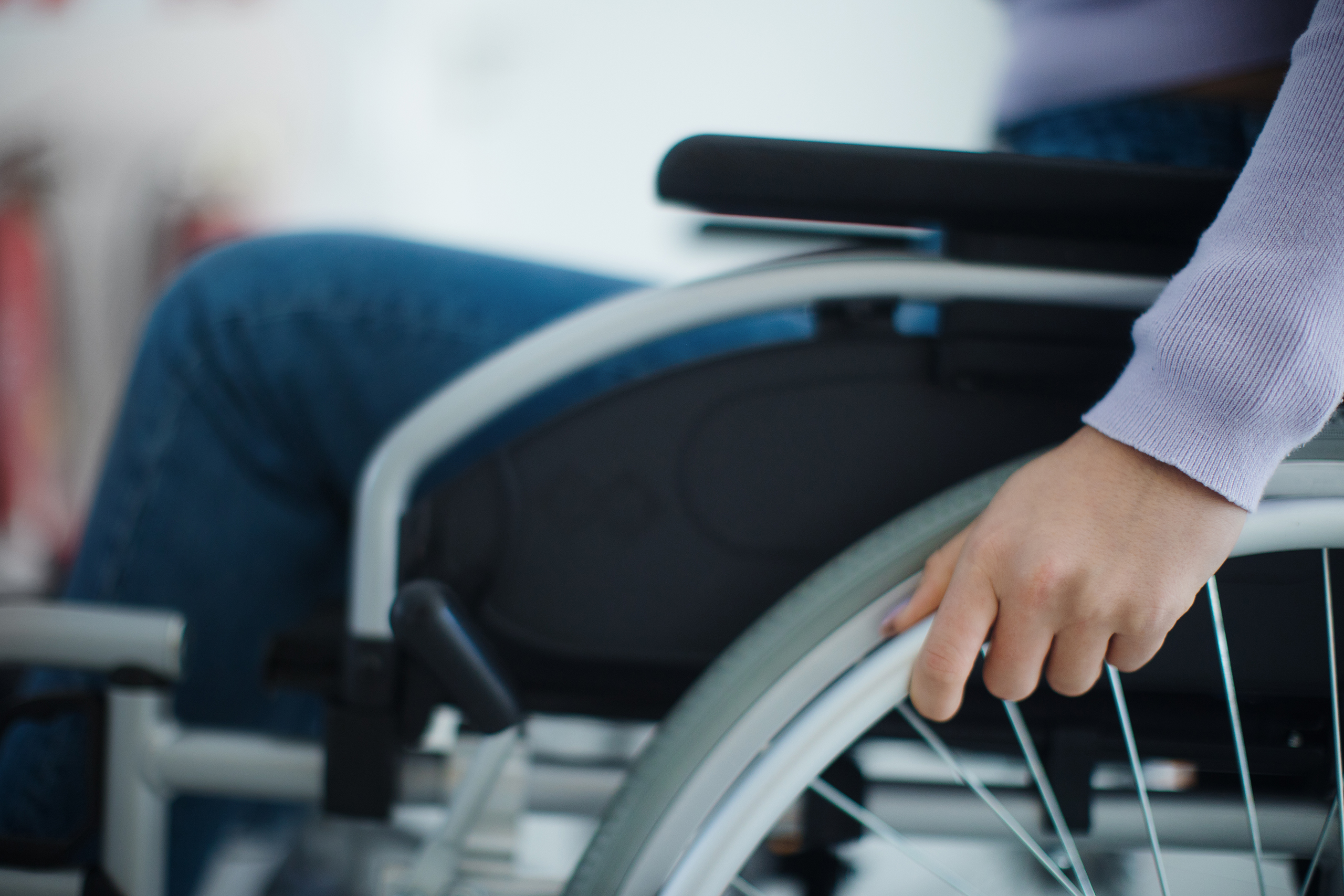 Close up of a wheelchair arm rest, and wheel with a hand on the wheel ready to move.