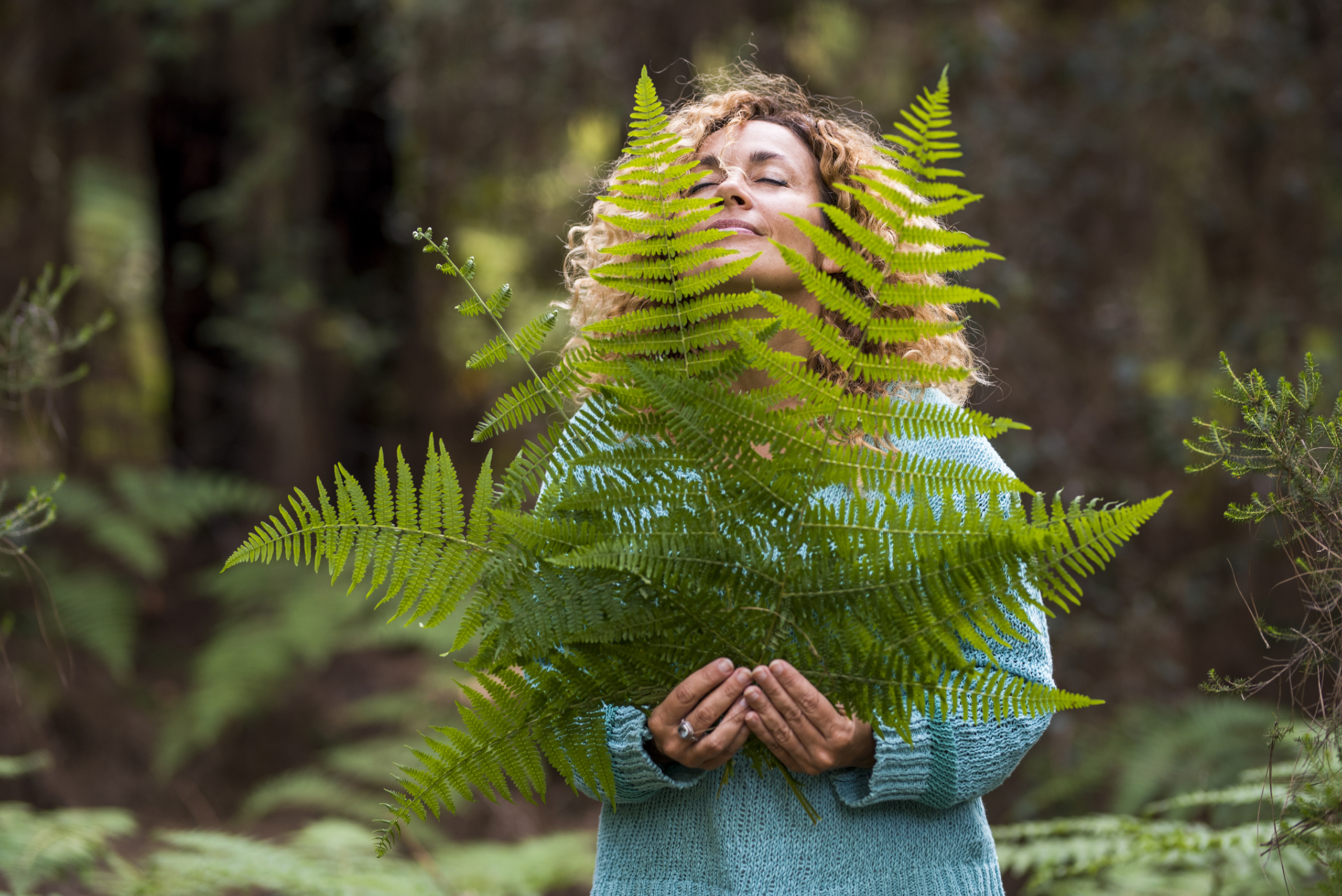 Woman with eyes closed looking up holding a large fern