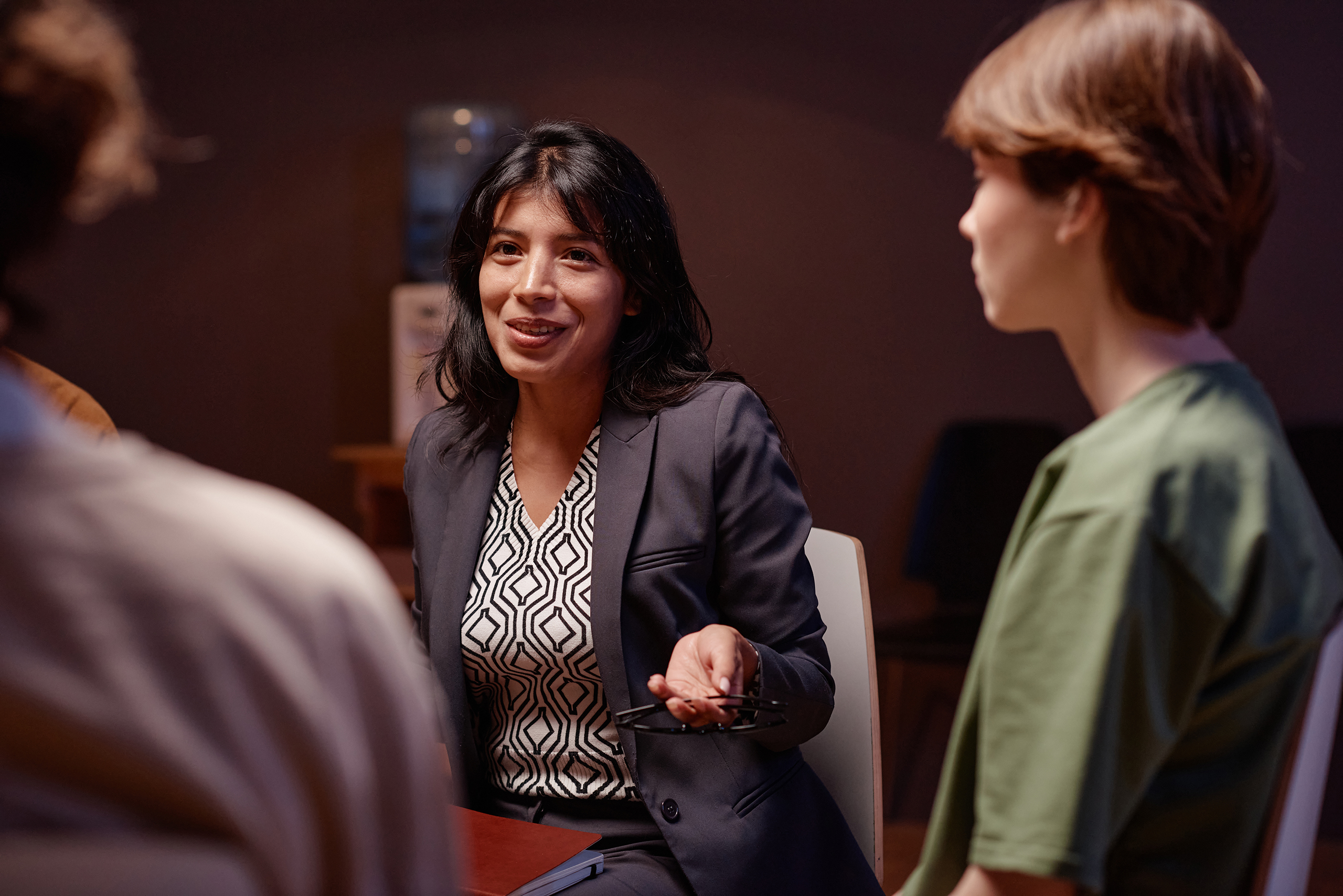 Three woman sitting having a group chat. Centre woman in focus running discussion, two women either side of her out of focus.