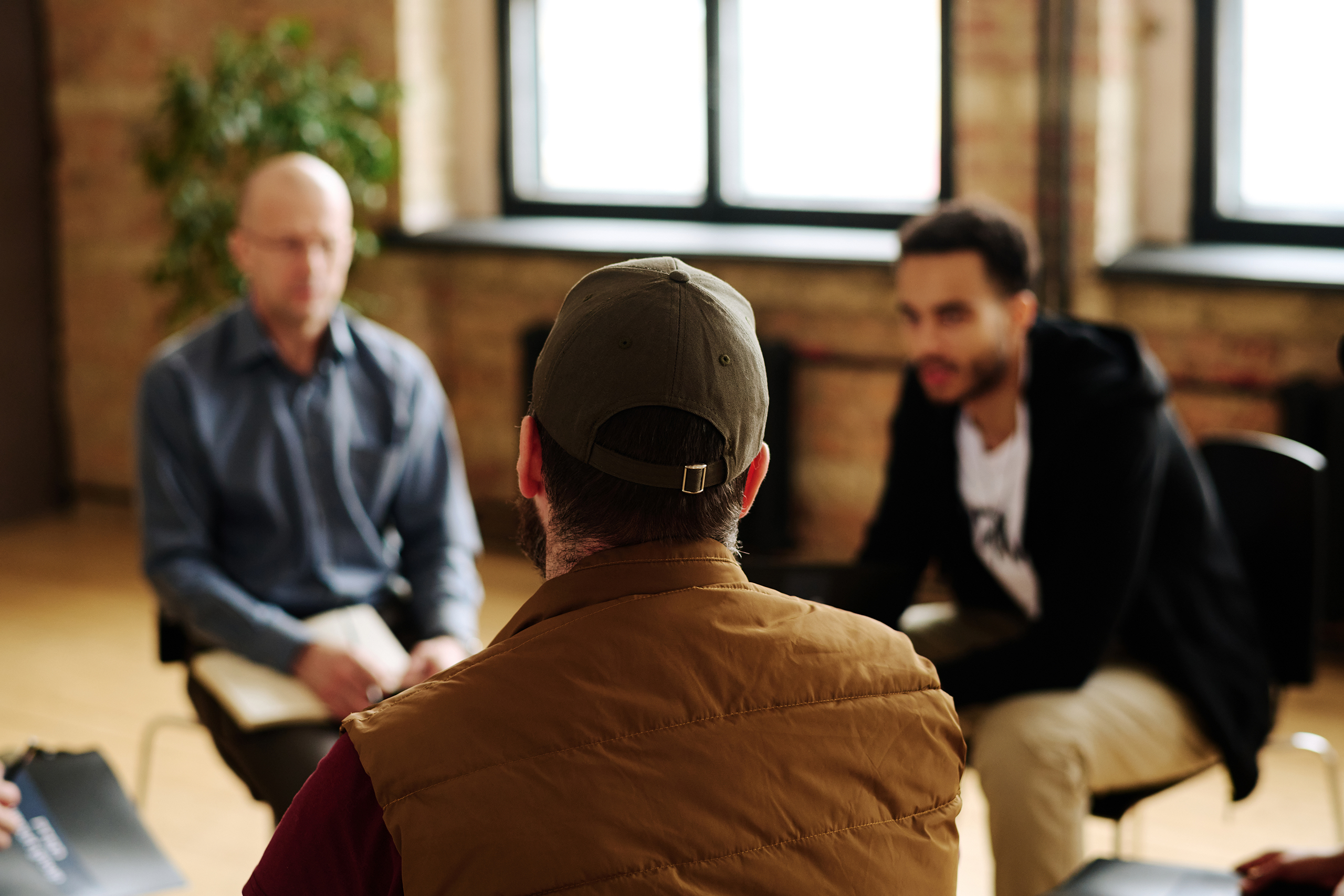 Three men sitting having a group chat. Two men out of focus and the back of one mans head.