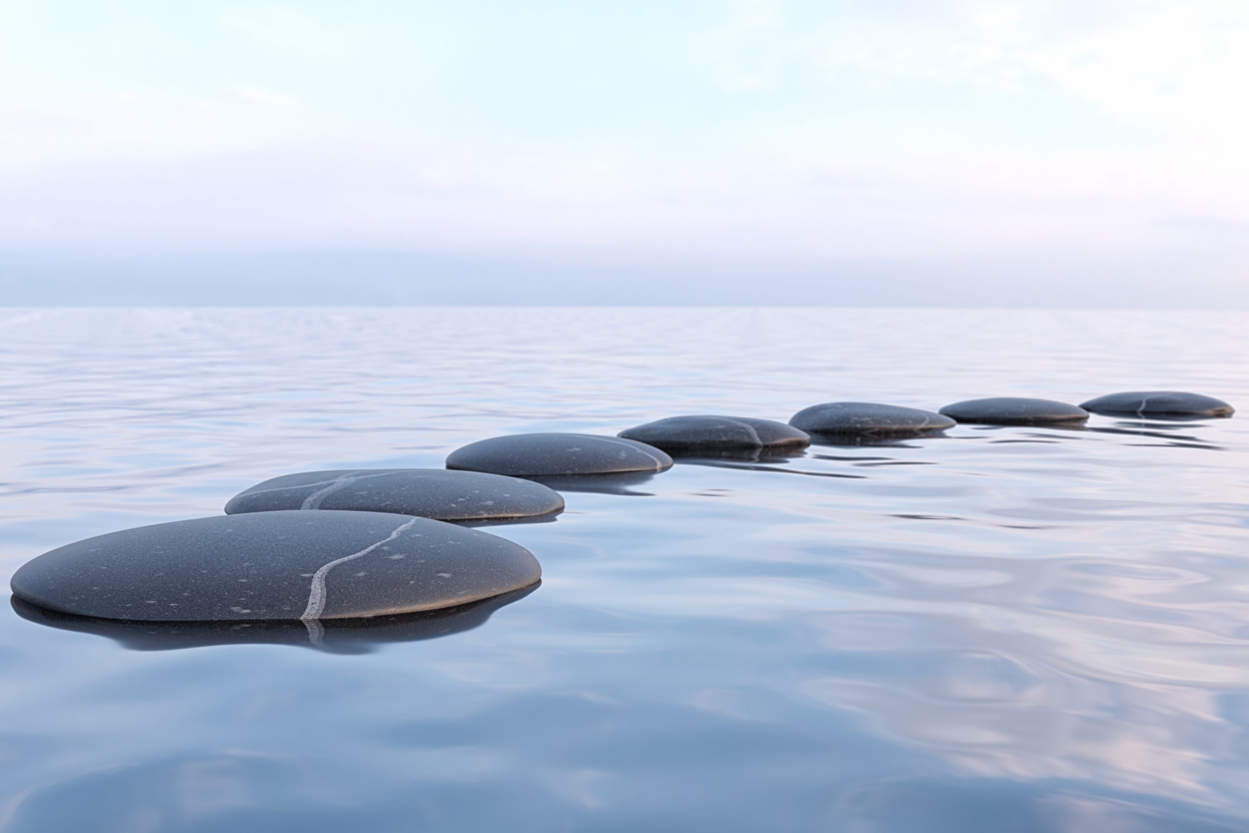 Six zen stones sitting just above the water in an arc formation.